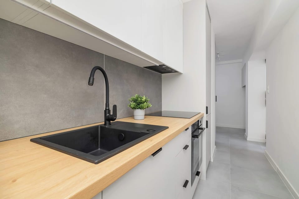 A kitchen sink area with a matte black tap, toaster, and tiled backsplash in a minimalist style.