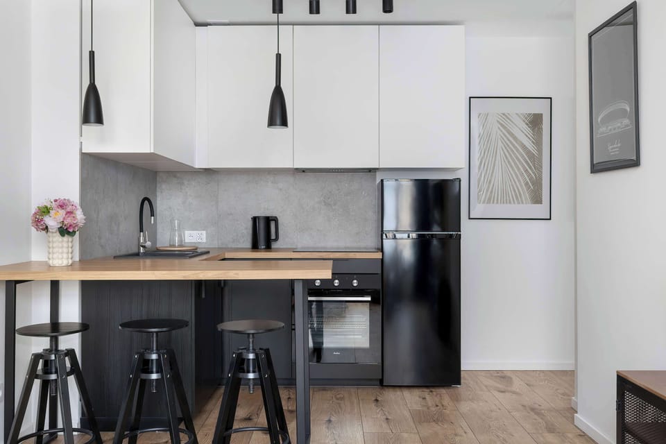 A compact modern kitchen with black stools, overhead lighting, and wooden elements. Perfect for cooking and casual dining.