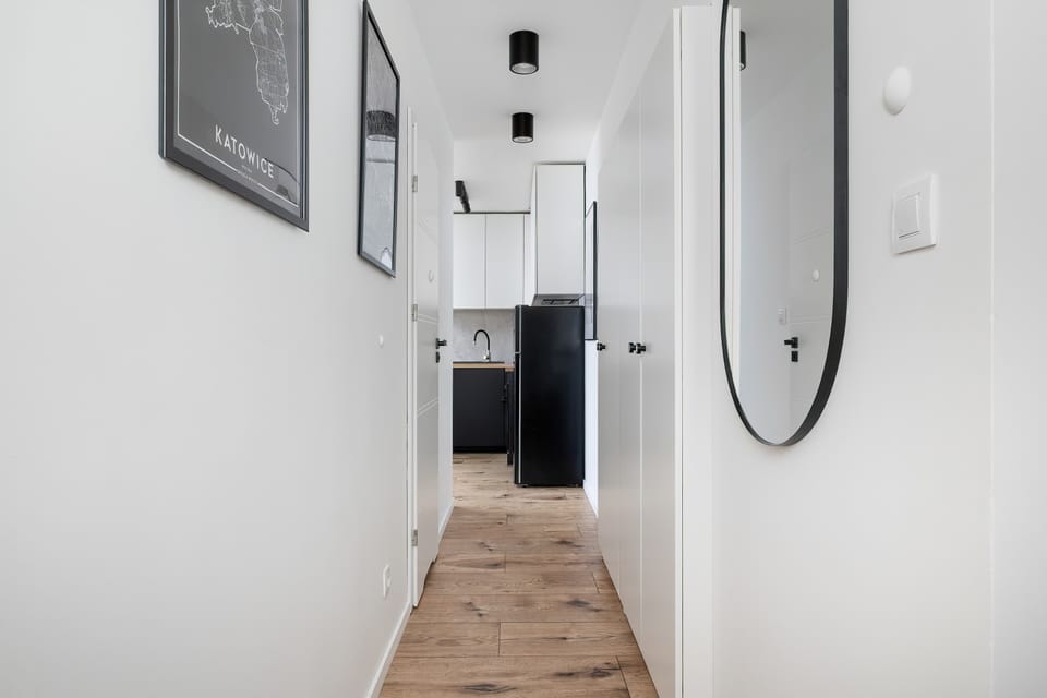 A long shared corridor with wood floors and bright white walls. Functional and simple, ideal for apartment access.
