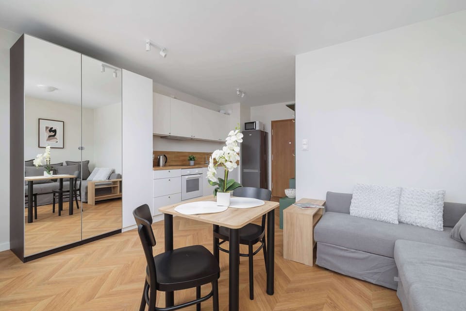Bright and cozy living space with a grey sofa bed, dining area, and access to the balcony.