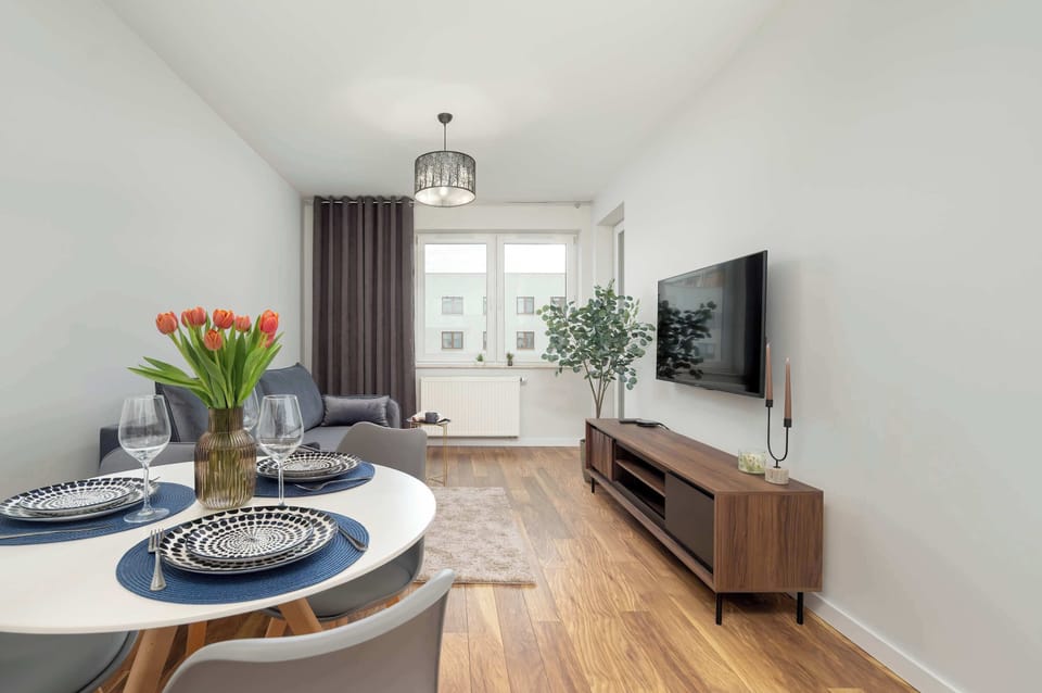 The spacious living room with large windows, grey sofas, and a TV offers a comfortable place to relax after a long day of exploring the city.