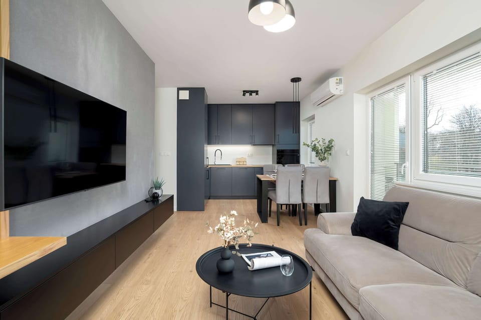 A different angle of the living room, highlighting the TV area with a wooden slatted panel and black shelving for a modern aesthetic.