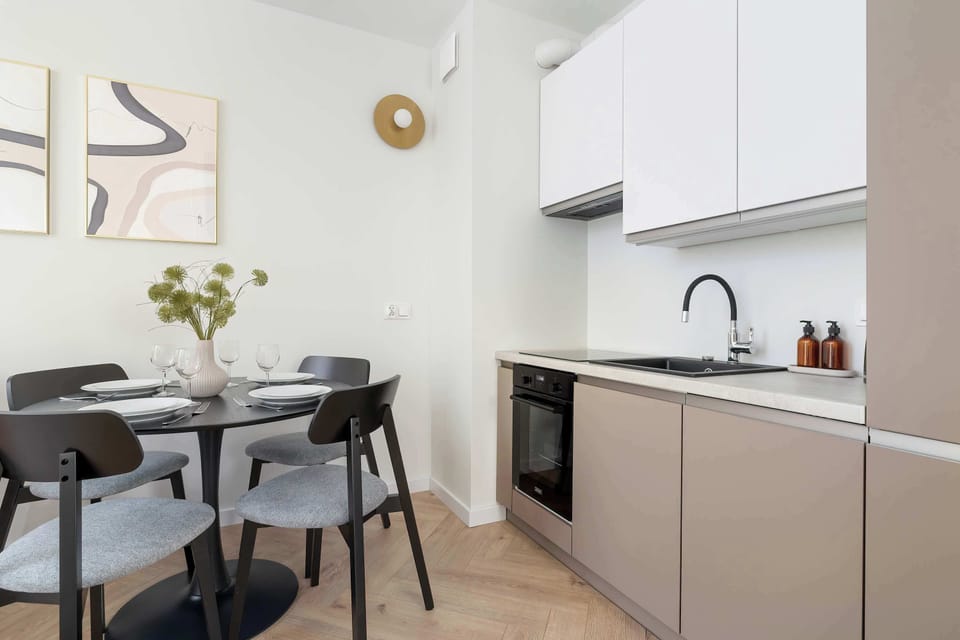 A compact kitchen with modern appliances and a dining table set for two. The neutral color palette creates a welcoming atmosphere.
