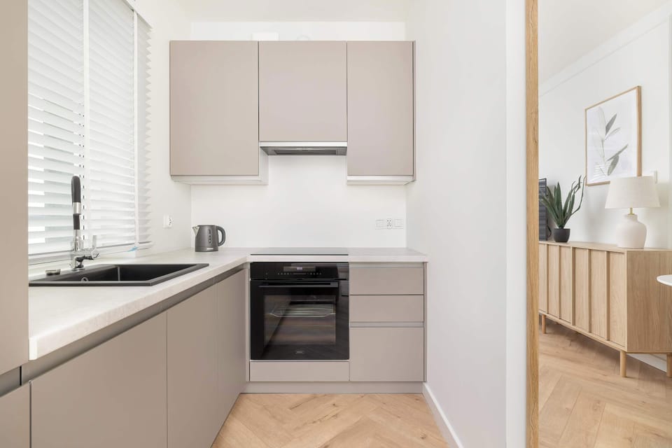 A compact kitchenette includes modern appliances, such as an oven and induction hob. The clean, neutral tones complement the rest of the apartment's contemporary style.
