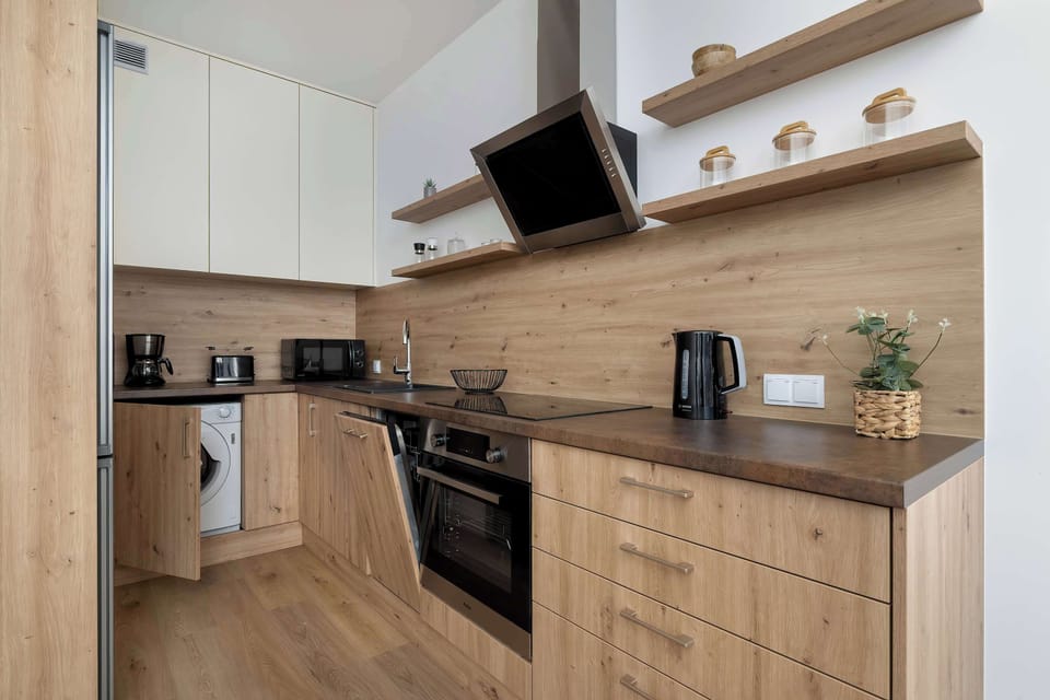A kitchenette open to the living room with wooden cabinets, appliances (oven, stove), and a shelf full of potted plants creates a harmonious and inviting space.