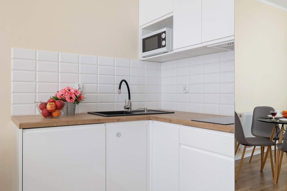 A compact and stylish kitchen with white cabinetry and modern appliances. A small countertop with a vase of flowers adds charm to the space.
