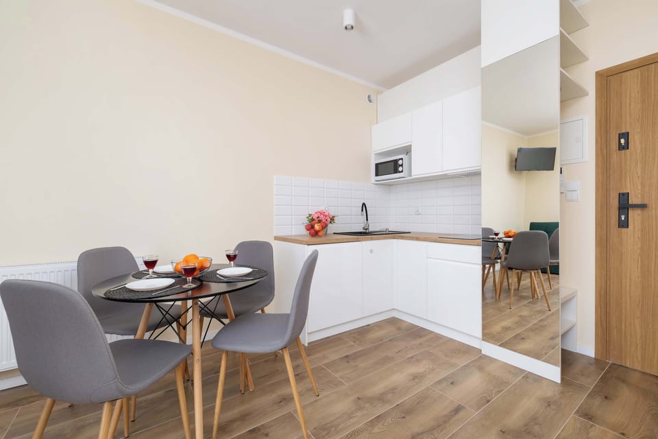 A bright open-concept kitchen and living room with a dining table. The minimalist decor and neutral colors make it feel inviting.