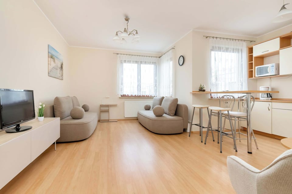 A spacious and bright living room with a large window letting in natural light, and comfortable armchairs and a sofa in muted shades of gray creates a pleasant space for relaxation.