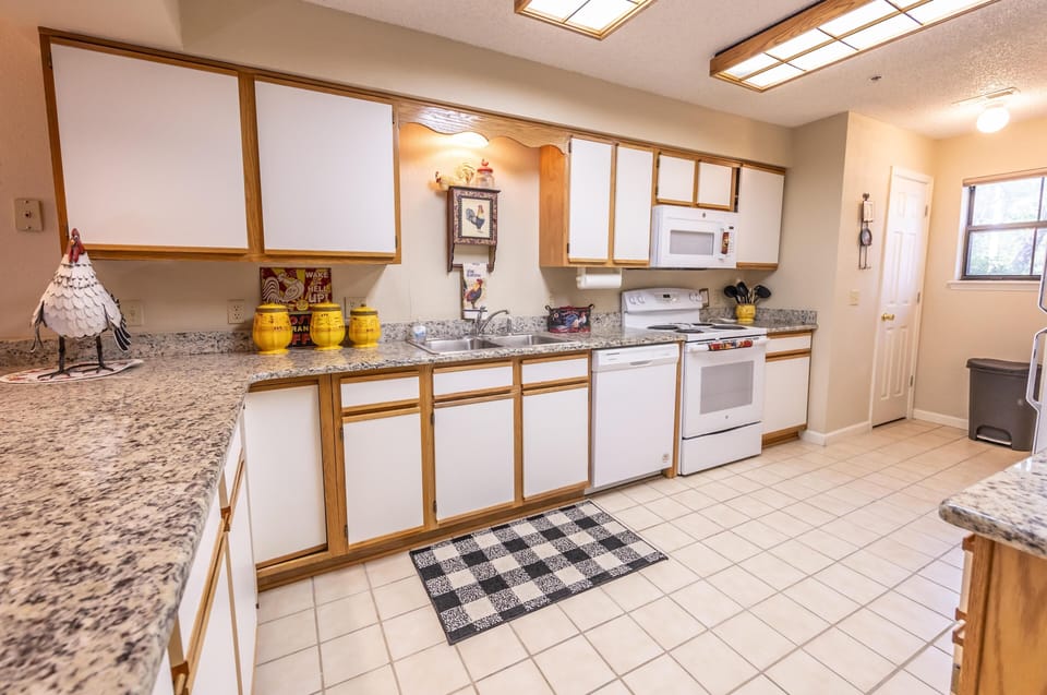 Kitchen with granite countertops, white appliances, dual sink, and wooden-trimmed cabinetry under fluorescent ceiling lights.
