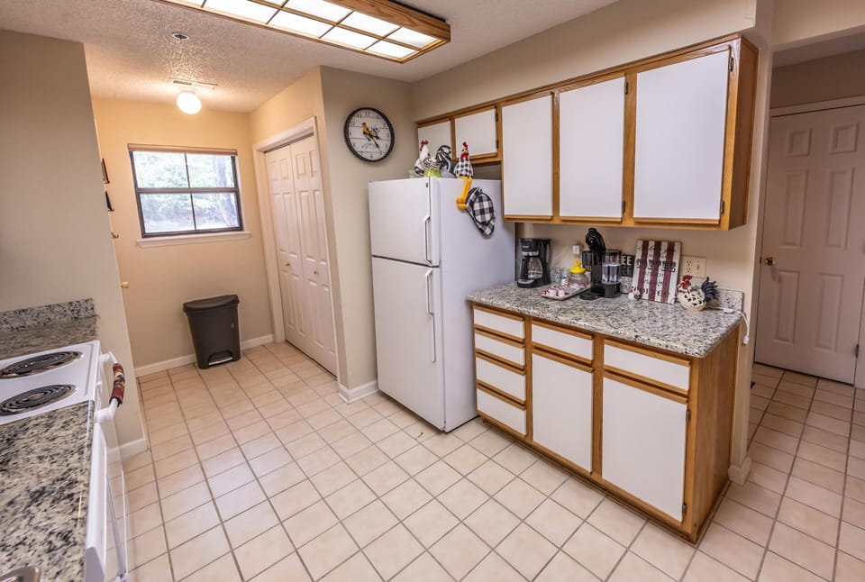 Galley kitchen with granite counters, white appliances, wood-trimmed cabinetry, tiled floor, and overhead fluorescent lighting.