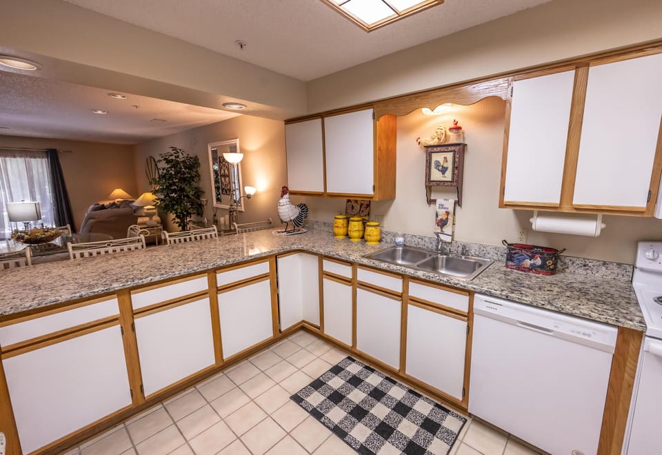 L-shaped kitchen features granite countertops, white and wood cabinetry, double sink, and tile flooring.