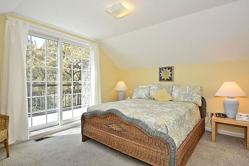 The upstairs bedroom is filled with natural light from large windows and features a king-sized bed, stylish decor, and a cozy atmosphere perfect for restful nights.