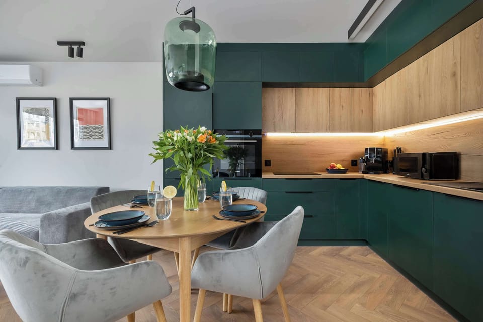 A stylish kitchen-dining combo with forest green cabinets, wooden accents, and a round table under pendant lighting.