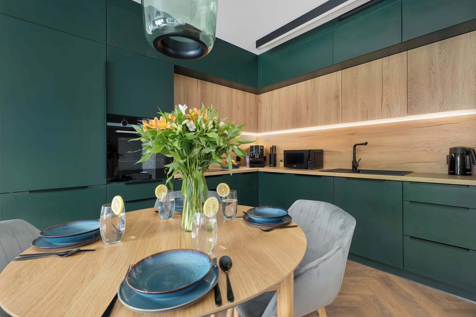 Another view of the dining area with a green-and-wood kitchen, rounded table, and stylish hanging light.