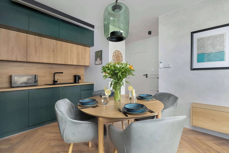 A kitchen with green cabinetry and natural wood countertops, featuring modern appliances and decor.
