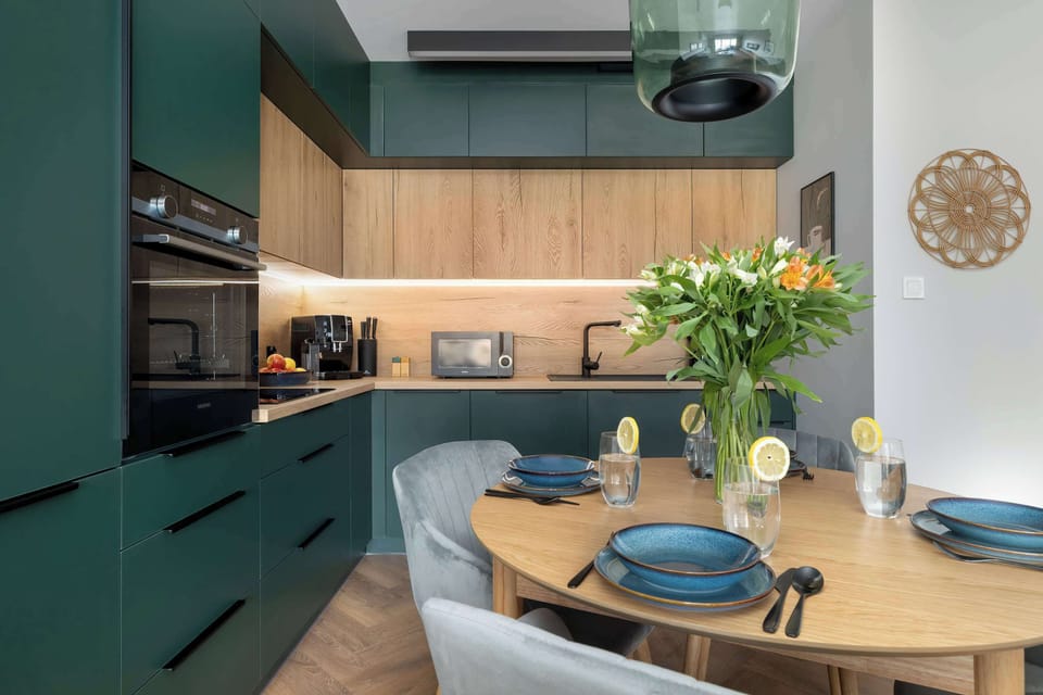 A stylish kitchen area with integrated appliances, green cabinetry, and a minimalist backsplash.
