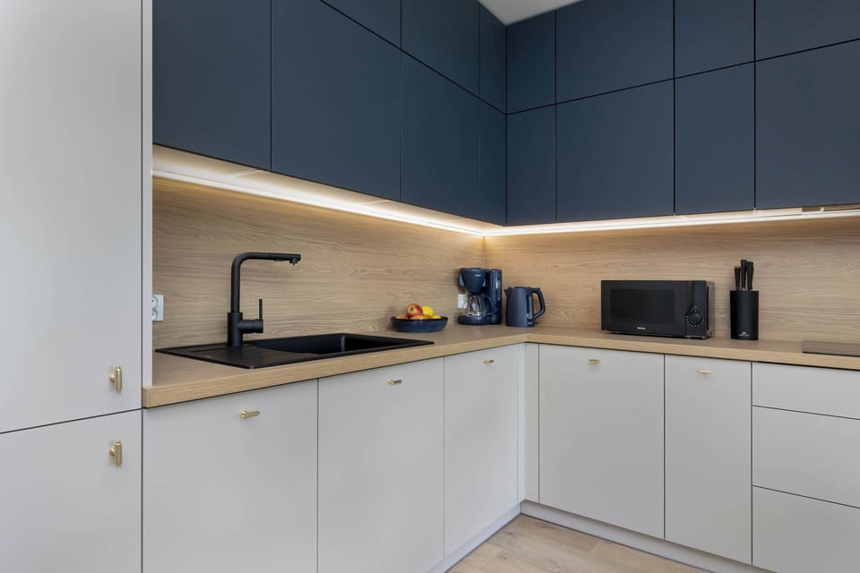 A compact and stylish kitchen with modern navy and white cabinetry, wooden countertops, and under-cabinet lighting.