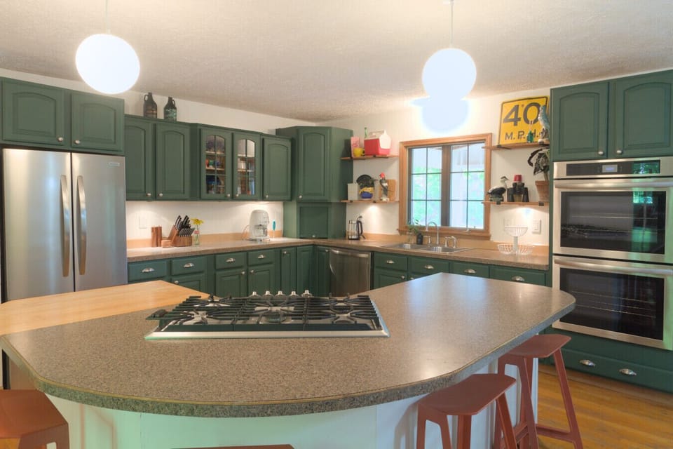 Chic kitchen with forest green cabinets and brand new appliances including a double oven cooking up some vintage camp charm 🌿🍽️ This fully stocked kitchen has everything you need, including ample plates, cutlery, cups, cutting boards, baking dishes, an ai