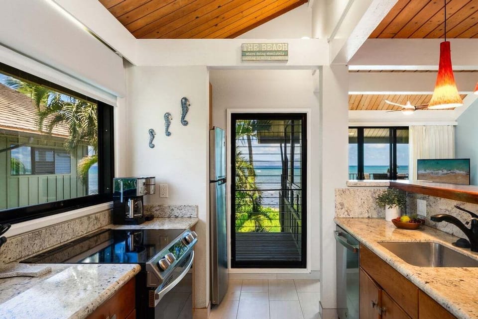 Bright kitchen with granite countertops, stainless steel appliances, and large windows overlooking tropical greenery