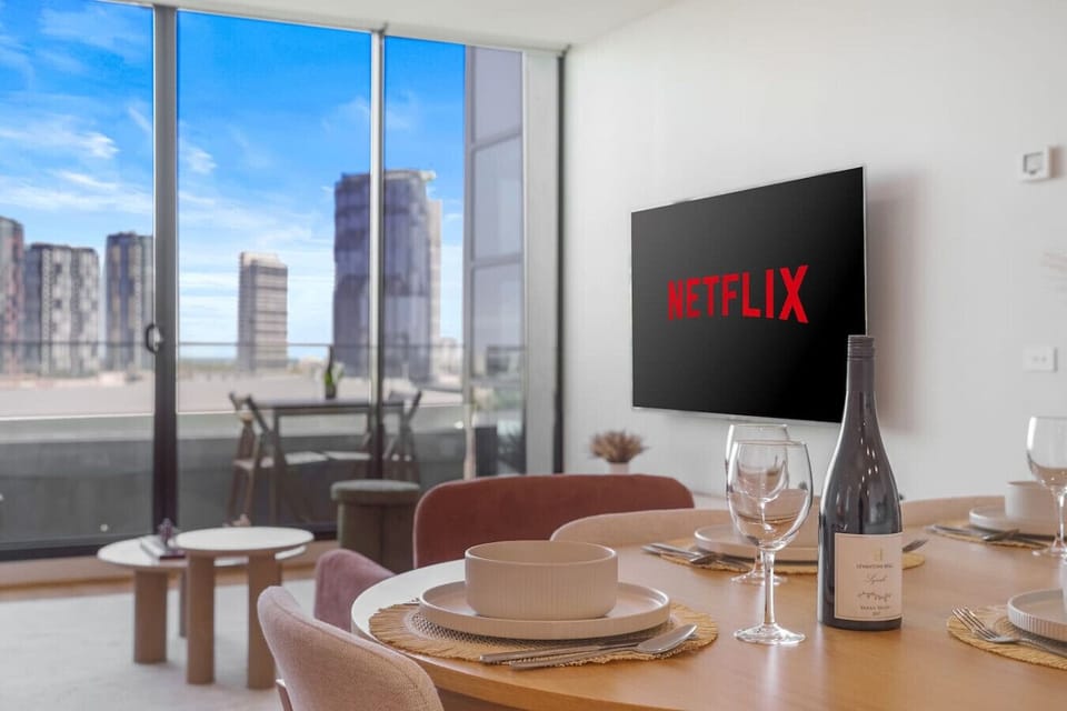 A stylish dining area set for a meal, complemented by a large TV and bright floor to ceiling views, creating a cozy space for dining and relaxing.