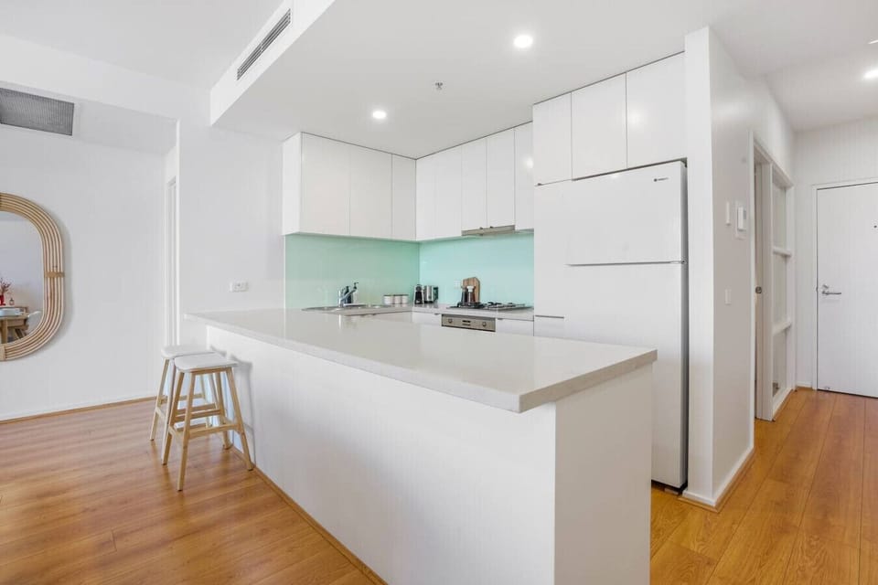 A bright, modern kitchen with a spacious island, sleek white cabinetry, and warm wood flooring, creating an inviting and functional space for cooking and gathering.