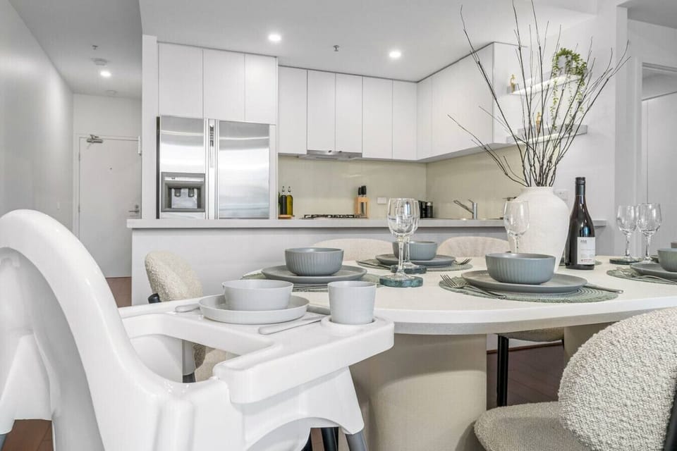 Elegant dining setup with modern tableware, a high chair for convenience, and a sleek kitchen backdrop featuring stainless steel appliances and clean white cabinetry.