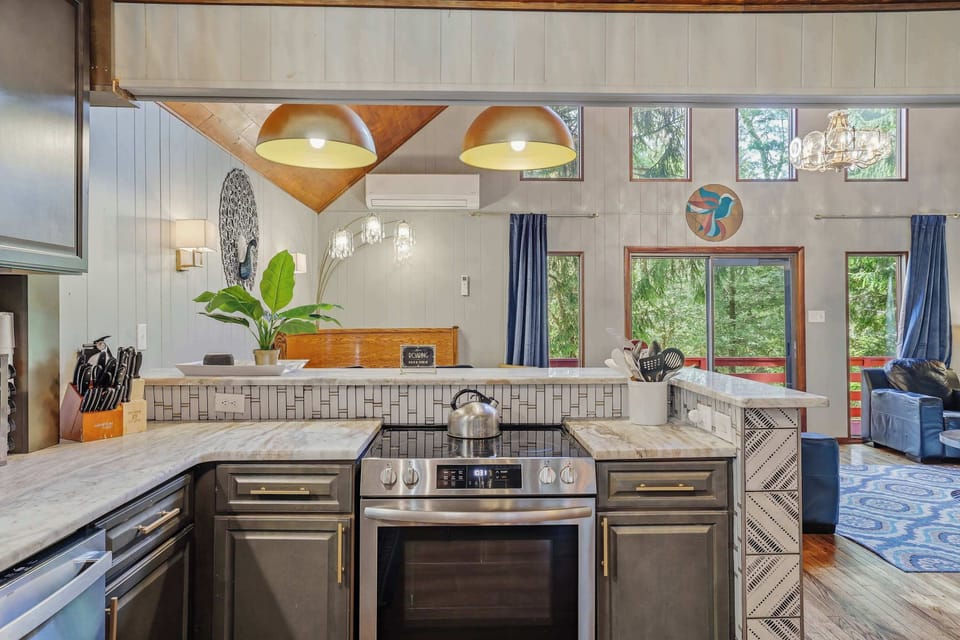 Cook something real in a kitchen that actually wants you to — stainless range, marble countertops, forest window view, and pendant lights that make
prep feel like part of the evening.