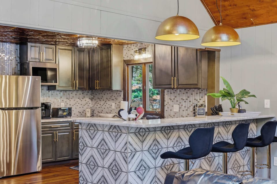 Sit at the geometric tile island for breakfast — stainless fridge behind you, pendant lights overhead. The day starts right here before it even starts.