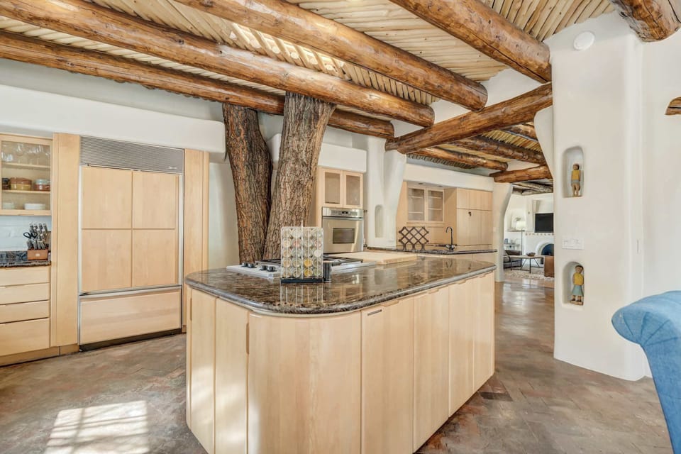 Hand-hewn ceiling beams and organic textures surround the kitchen and dining space, where indoor trees and adobe curves create a one-of-a-kind atmosphere. This open-concept area is both functional and full of character.

