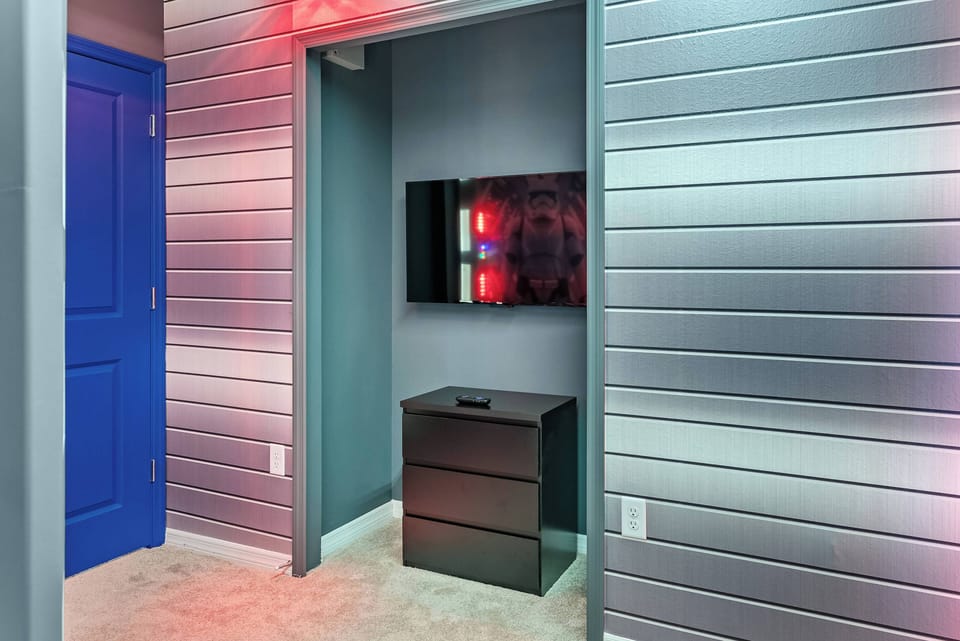 Discover a unique spot in this property, where a sleek flat-screen TV sits above a modern dresser, all accented by stylish silver paneling. The vivid blue door adds a cheerful touch, inviting you to unwind and relax.