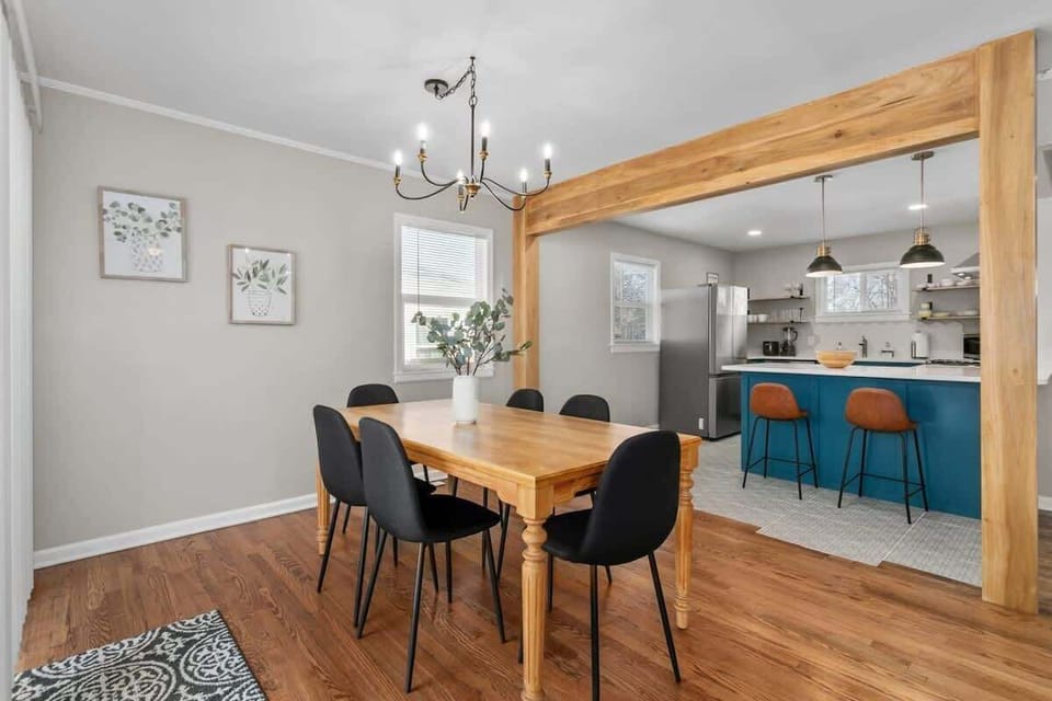 The room is bathed in natural light from the large windows, creating a warm and inviting atmosphere. The black chairs add a touch of modern style, while the chandelier provides elegant lighting.