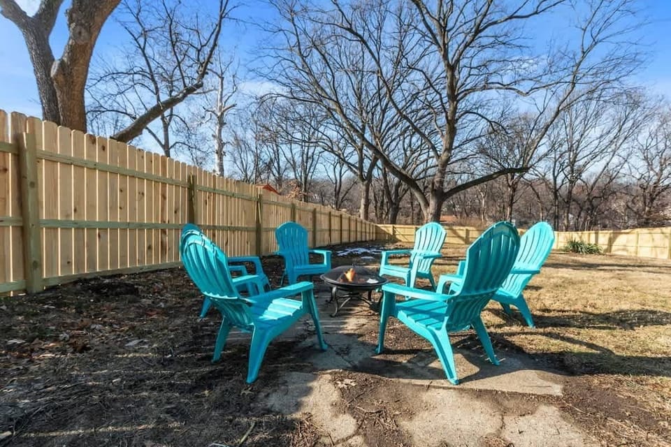 The backyard features a fire pit surrounded by four turquoise Adirondack chairs, inviting you to gather around and enjoy the warmth on cool evenings. 