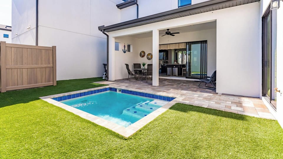 Covered patio with seating area overlooks a private pool and artificial grass lawn.