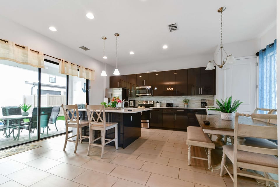 Modern kitchen with dark cabinetry, stainless steel appliances, and a bright dining area opening to an outdoor patio.