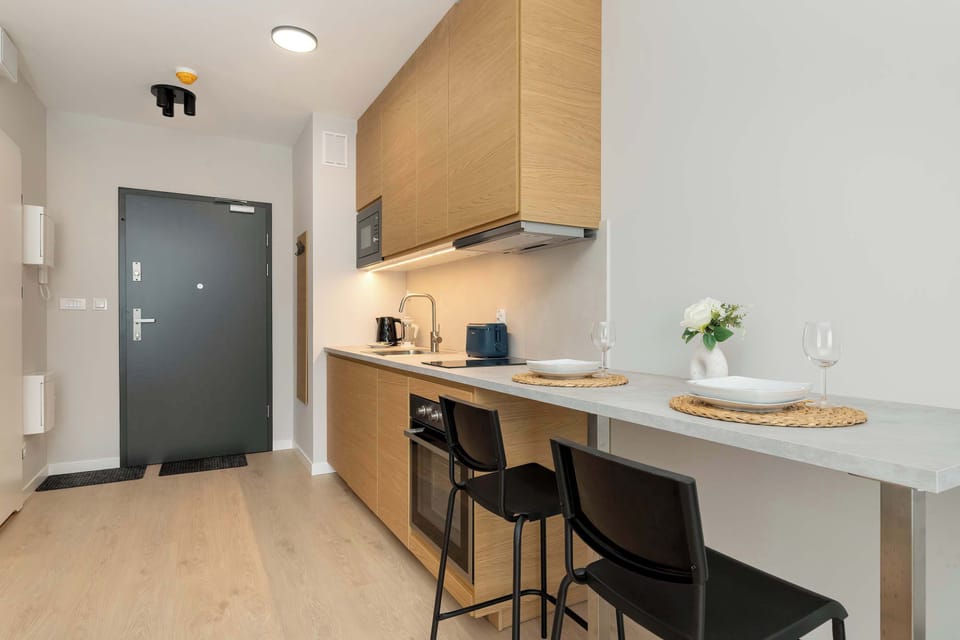 A compact entryway with light wood cabinetry and a workspace area featuring a chair and desk under warm lighting.
