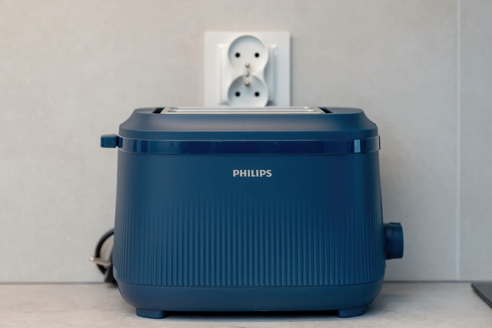 A blue toaster on a wooden floor against a white wall.