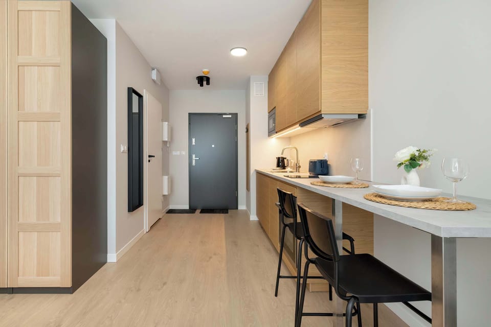 A small hallway with a desk and two stools, placed next to a wooden kitchenette with subtle lighting.