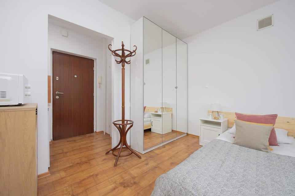 A bright, neat hallway leading to the apartment, with the entrance door on the left and a large mirror at the end.