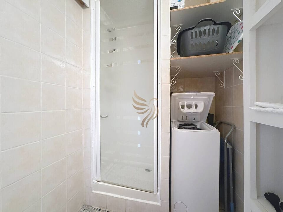 Salle de bain avec douche, vasque, rangements et lave-linge.