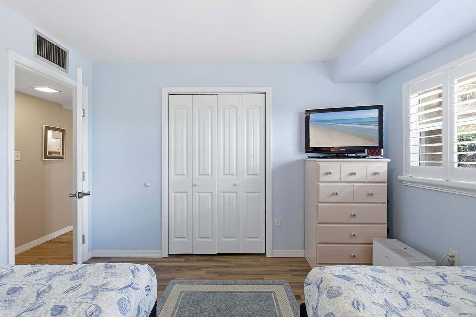 Bright beach stay bedroom with two beds, TV, and ample storage. Enjoy a clean, coastal feel and relaxing space—perfect for unwinding after a fun day by the ocean with family or friends.