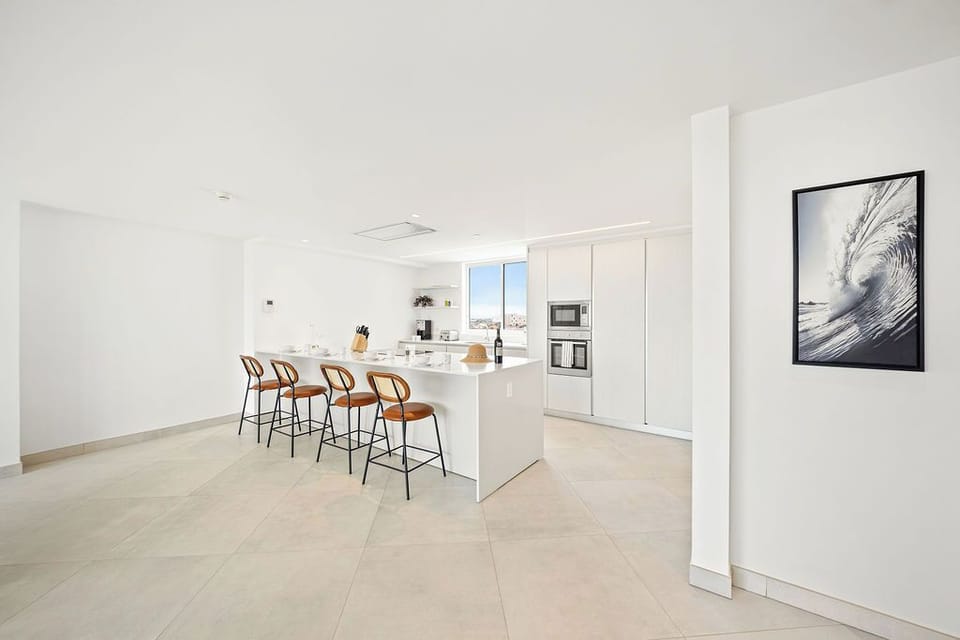 Gather with friends around the sleek island in this bright modern kitchen, where warm wood stools and ocean-inspired artwork set a relaxed coastal vibe.