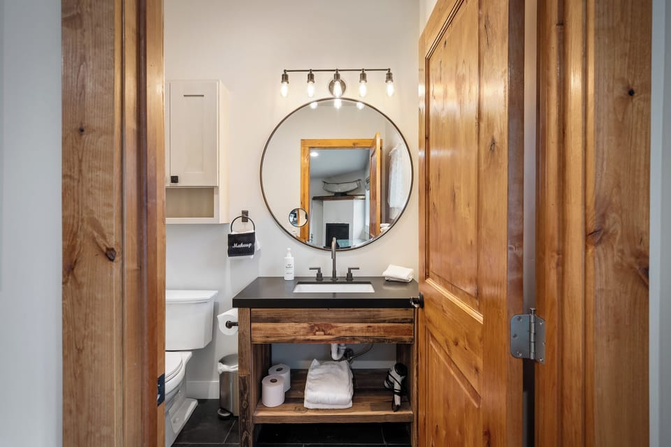 - Rustic bathroom with wood vanity and modern round mirror lighting   - Black countertop and open shelving offer style with functionality   - Cozy mountain touch combines modern features with cabin character