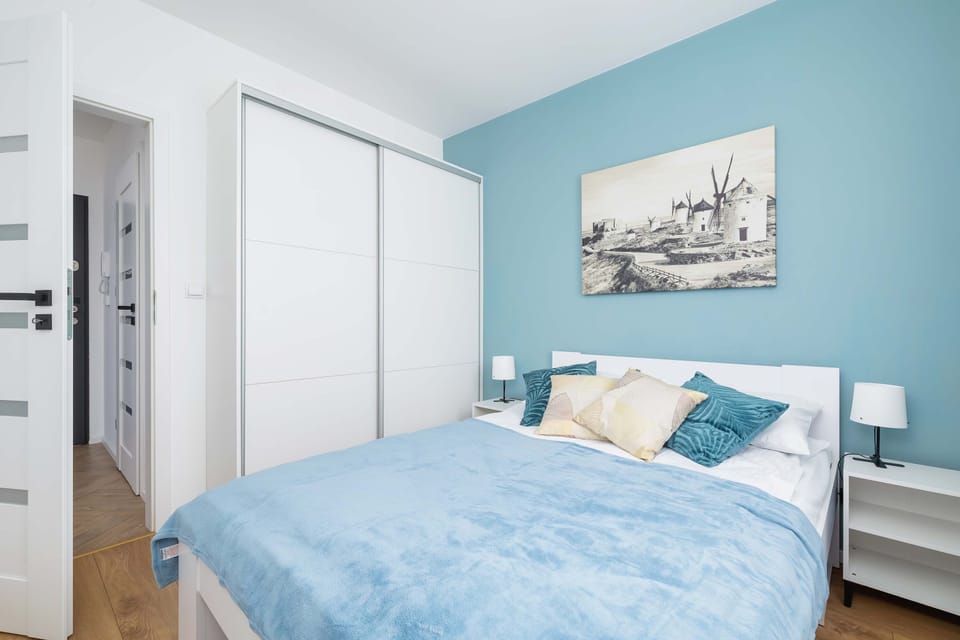 A cozy bedroom with a large bed covered in blue bedding and a painting above the headboard creates a calm atmosphere for sleep.