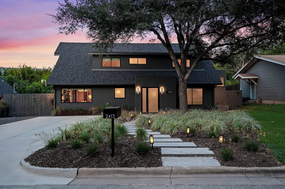 complemented by a beautifully manicured front yard featuring a meandering stone walkway, lush grasses, and accent lighting that creates a welcoming glow at dusk.