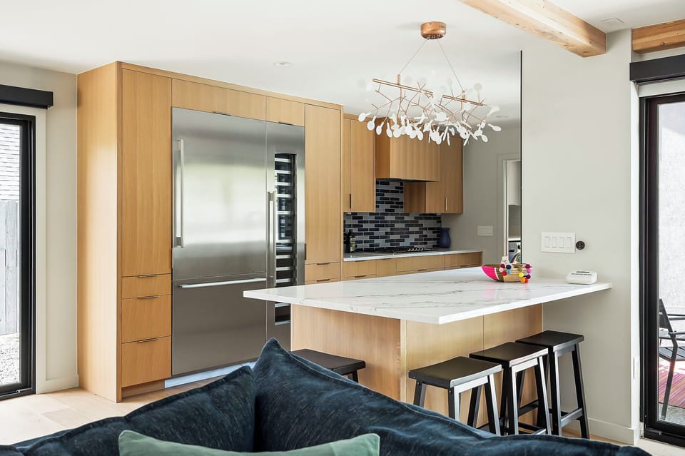 Another angle of the kitchen island and bar area, spotlighting the built-in refrigerator and dark stone backsplash behind the stovetop.