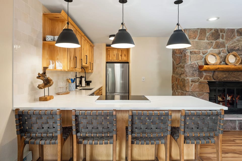 Your gourmet kitchen features warm wood cabinetry, sleek pendant lighting, and a stunning stone fireplace perfect for cozy evenings.