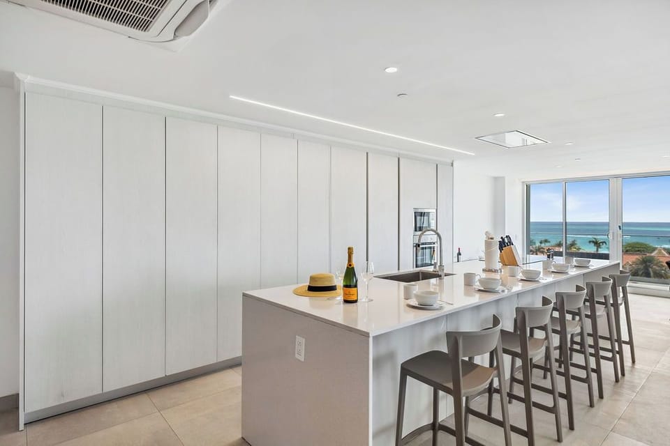 This bright, open kitchen features sleek design with island seating and stunning ocean views beyond, perfect for preparing meals and enjoying coastal breezes.