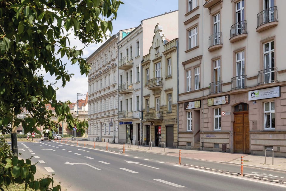  A street with classic buildings featuring large windows and ornate details on the right, and trees on the left, creates a calm urban landscape.