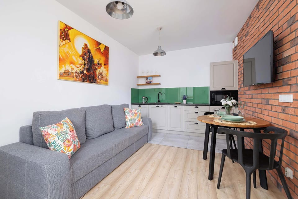 A cozy living room with a brick wall, colorful cushions on the sofa, and artwork on the wall radiates warmth and a homely atmosphere.
