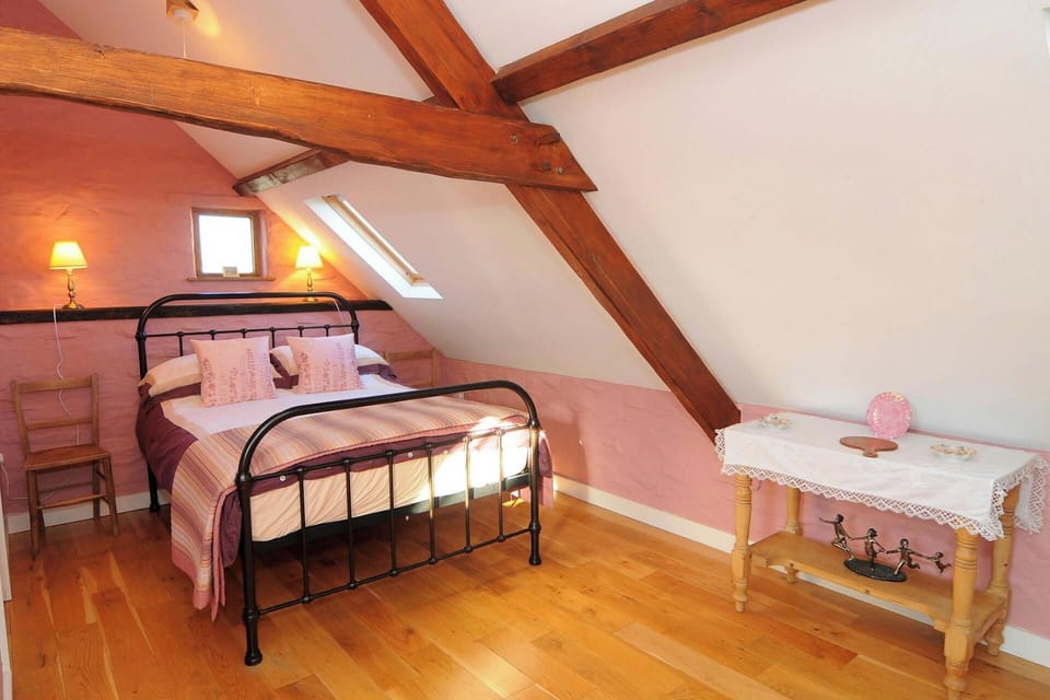 Double bedroom with exposed beams, table and wooden chairs with lamps on shelf behind the bed